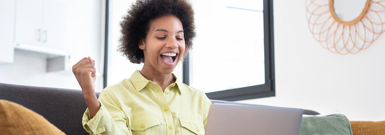 very attrractive young African American woman on the sofa pumping her fist maybe because she has won on her laptop computer