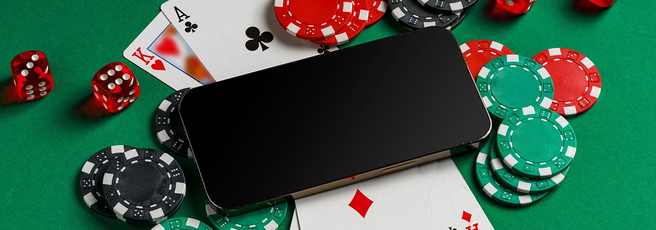 a smartphone on top of playing cards, with dice and casino chips around it on a green felt background