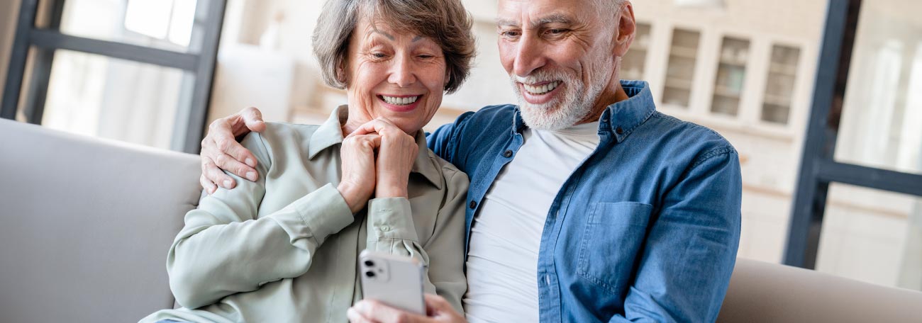 a smiling older couple comfortably together on the sofa enjoying the images on their mobile device