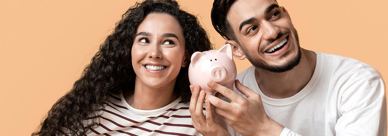 an attractive young couple listening to the sound of money jostling in their piggy bank