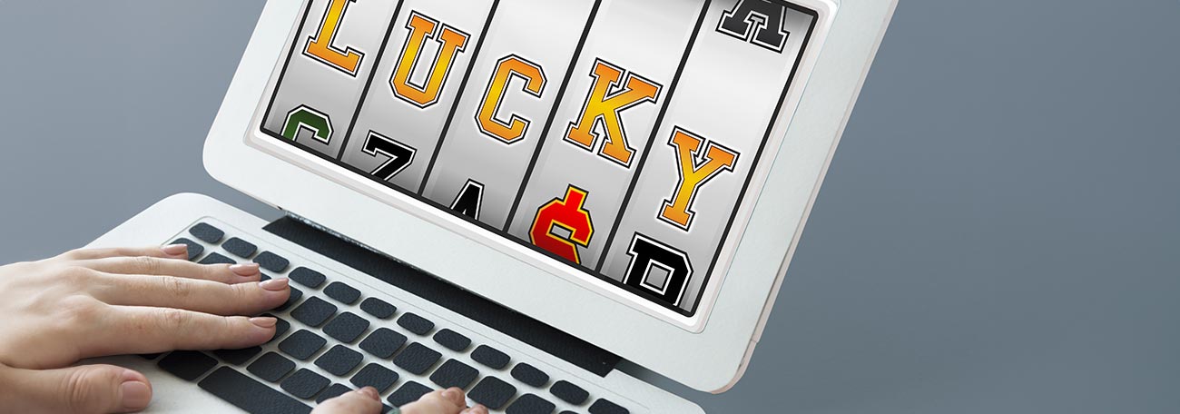 A woman's hand at a laptop keyboard with a five reel slot on the screen spelling out the word 