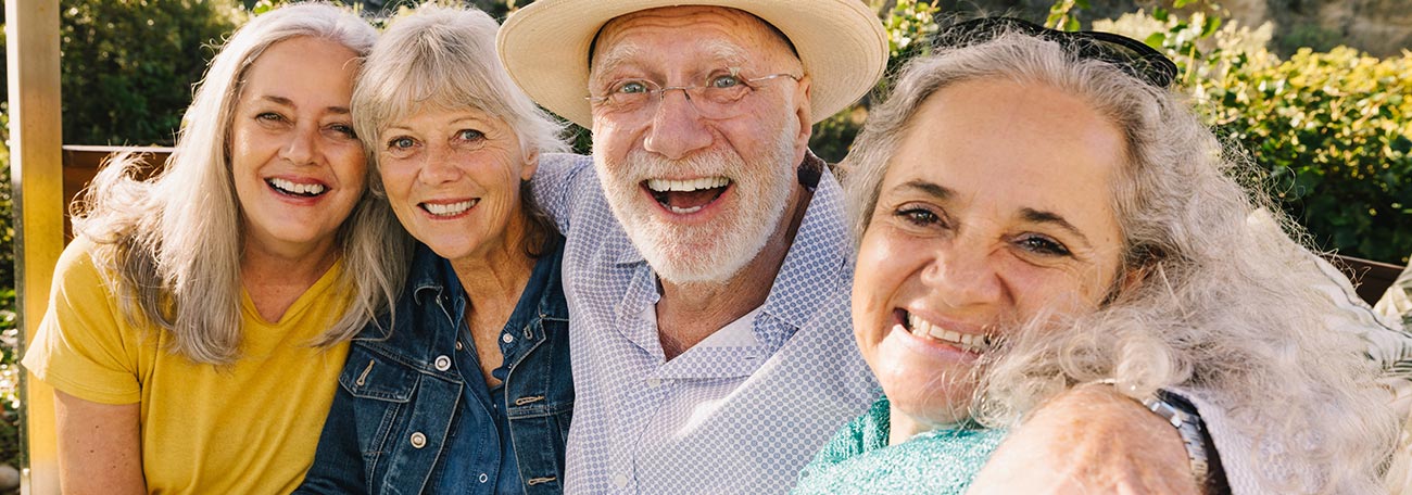 four older people, a man and three women, having fun outdoors with very broad smiles 